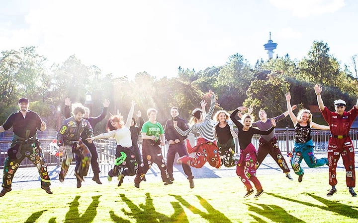 Students jumping into the air near Tammerkoski. The sun is shining and Näsinneula is visible in the background.